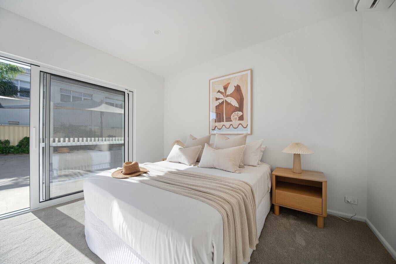 A bedroom with a bed, a nightstand, a lamp, a window, and a door.