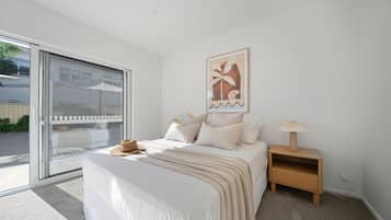 A bedroom with a bed, a nightstand, a lamp, a window, and a door.
