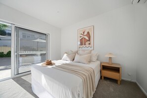 A bedroom with a bed, a nightstand, a lamp, a window, and a door. - Esplanade Apartments | Ocean View Beachfront | West Beach (West Beach)