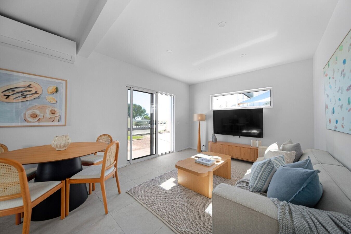 A modern living room with a dining area, a flat-screen TV, and a large window.