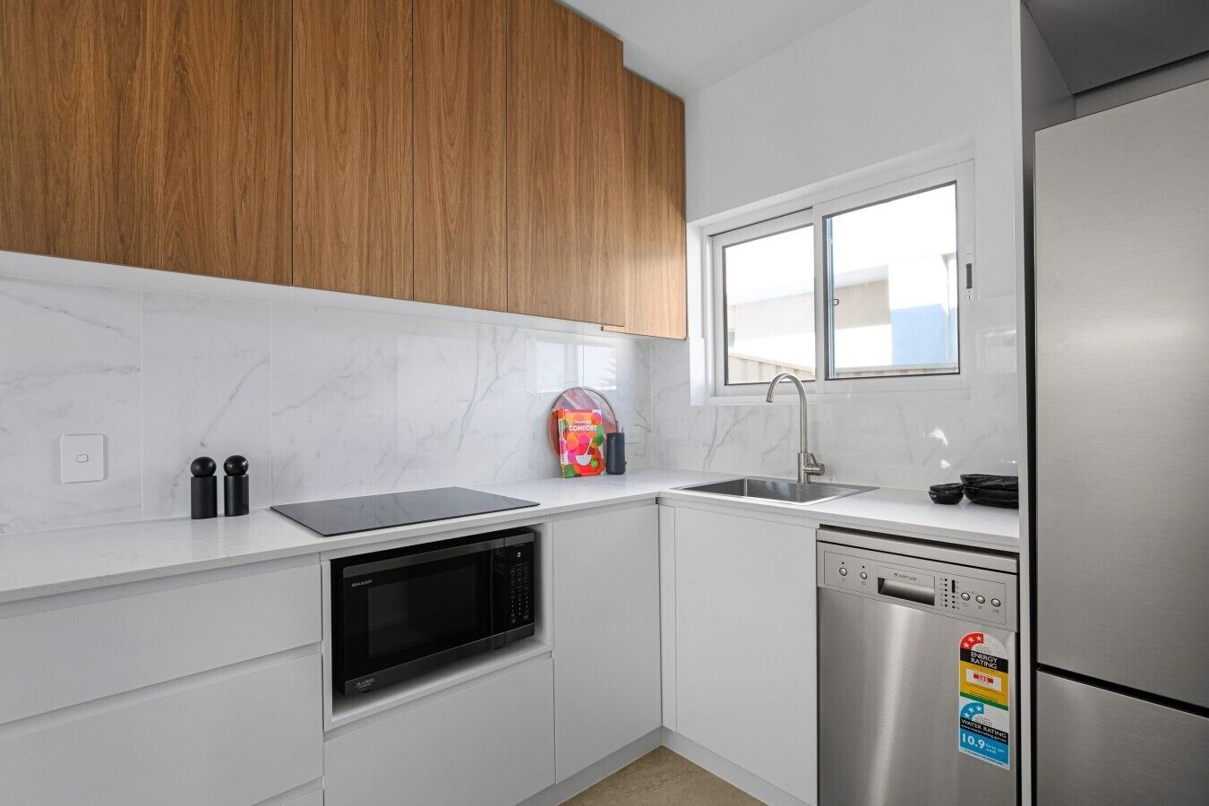 A modern kitchen with white cabinetry, a built-in microwave, a dishwasher, and a stainless steel refrigerator.