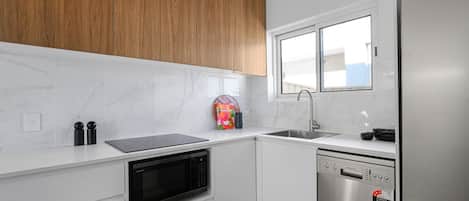 A modern kitchen with white cabinetry, a built-in microwave, a dishwasher, and a stainless steel refrigerator.