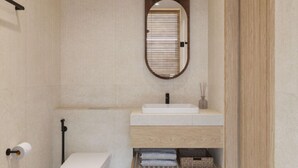 Une salle de bain avec des toilettes blanches, un miroir à cadre en bois et un lavabo blanc avec une étagère en bois en dessous.