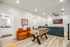 Ein modernes Wohnzimmer mit einem Kicker, einer Couch, einem Esstisch und einer Küchenzeile mit Spüle und Spiegel.