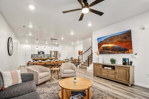 A spacious living room with a dining area, a kitchen in the background, a ceiling fan, and a large landscape painting on the wall. - Desert Haven, Private Spa, Community Amenities w/ Water Slide (Hurricane)