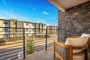 Un balcon avec un mur en pierre, une vue sur un immeuble à plusieurs étages et un véhicule garé.