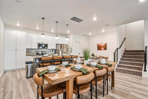 Une cuisine moderne avec des meubles blancs, des appareils en acier inoxydable et un coin repas doté de tables en bois et de chaises en cuir.