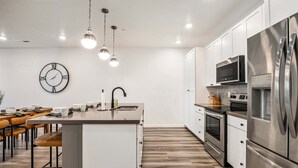 A modern kitchen with a central island, stainless steel appliances, and a dining area with wooden chairs. - Desert Haven, Private Spa, Community Amenities w/ Water Slide (Hurricane)