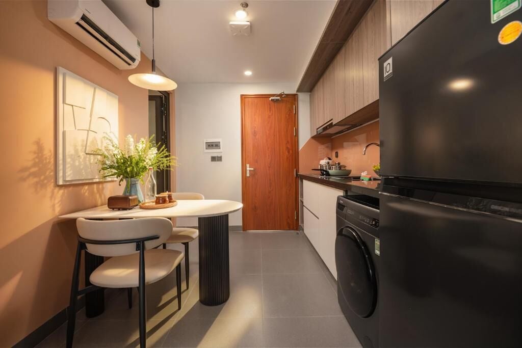 A compact kitchen with a washing machine, a dining area with a table and chairs, and a wooden door.