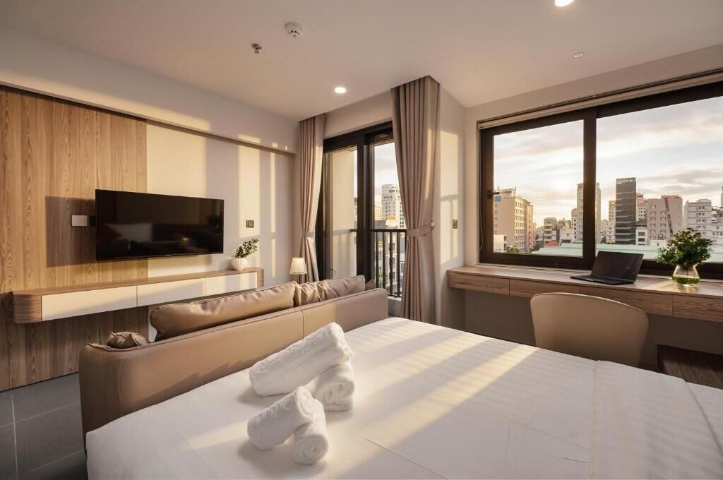 Une chambre d’hôtel moderne équipée d’un lit, d’un bureau, d’un ordinateur portable, d’une télévision et offrant une vue sur la ville.