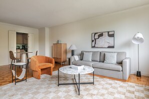 A living room with a sofa, armchair, coffee table, and a dining area with chairs and a table. - Blueground | Fenway–Kenmore, fitness, nr Fenway Park (Boston)