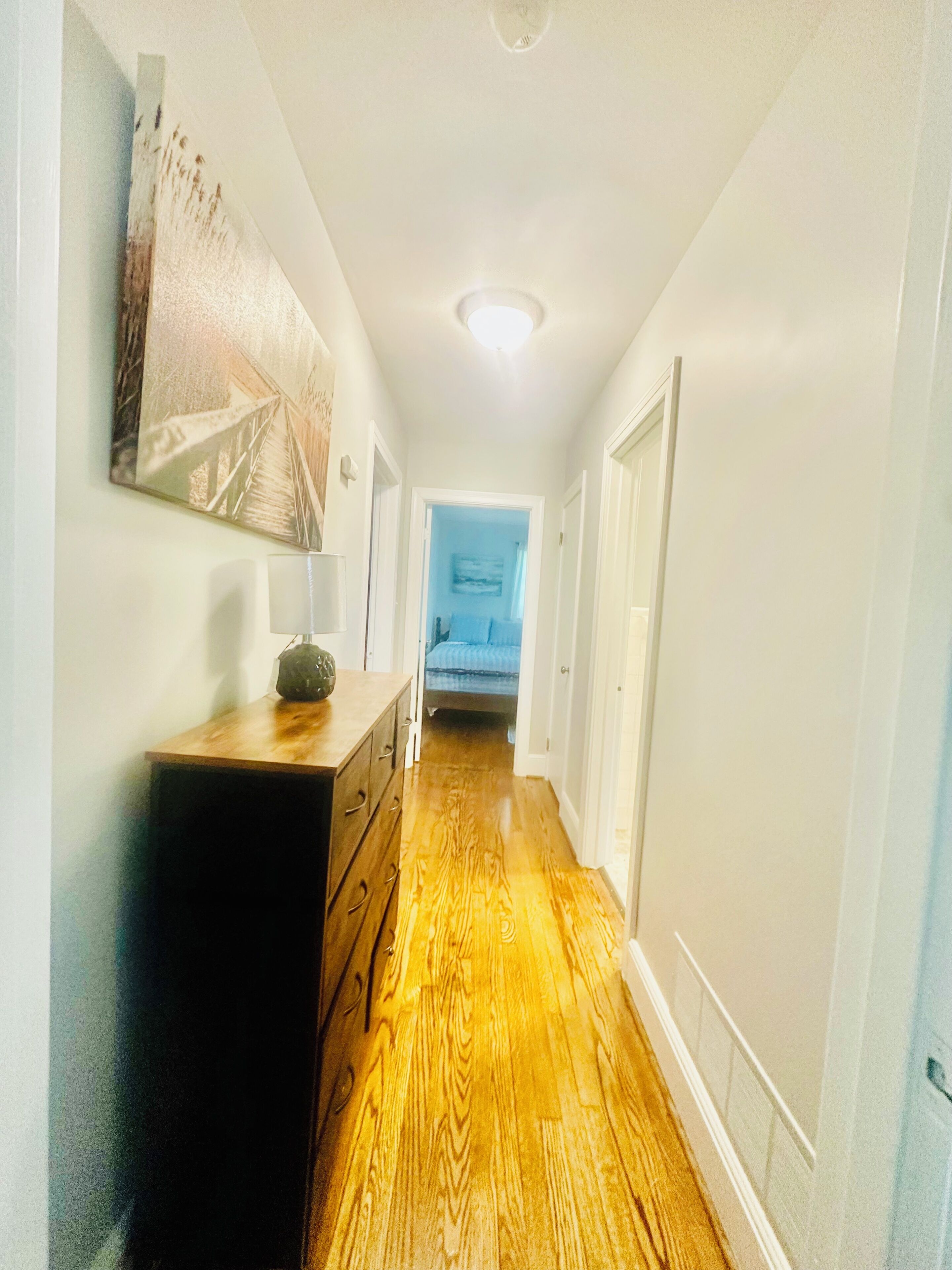 Un pasillo con piso de madera, un aparador y un cuadro en la pared.