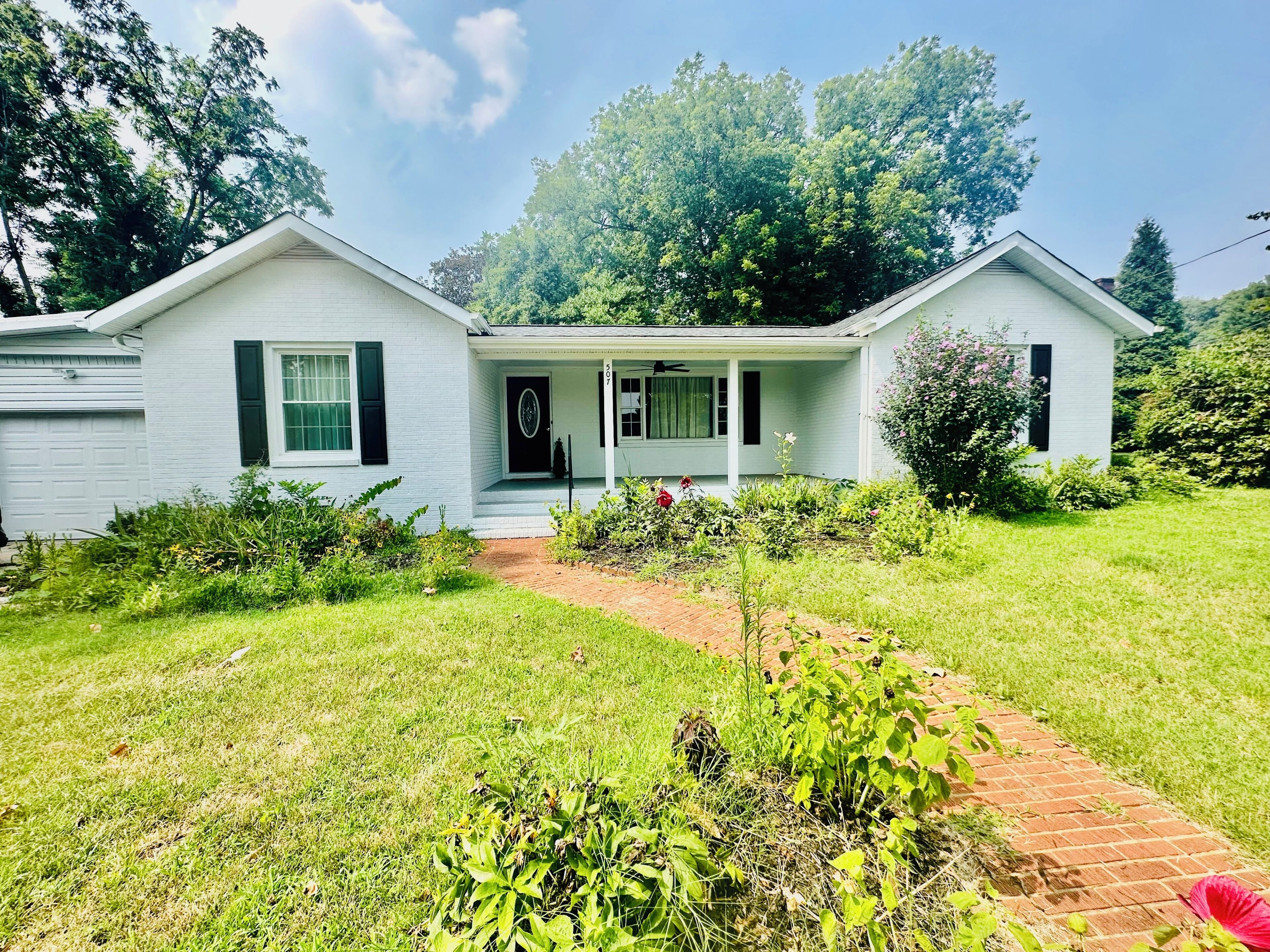 A two-story white house with a front porch, a brick pathway, and a well-maintained lawn.