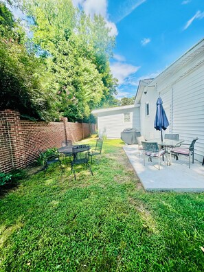 A backyard with a patio area, a brick wall, and a white building. - 4BR/3BTH Home in Eden, NC -Near Berry Hill Megasite & Martinsville Speedway (Eden)