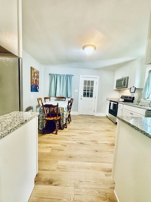 A kitchen with a dining area, wooden chairs, a table, and a door. - 4BR/3BTH Home in Eden, NC -Near Berry Hill Megasite & Martinsville Speedway (Eden)