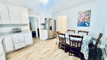 Una cocina compacta con armarios blancos, un refrigerador y un comedor con mesa y sillas.