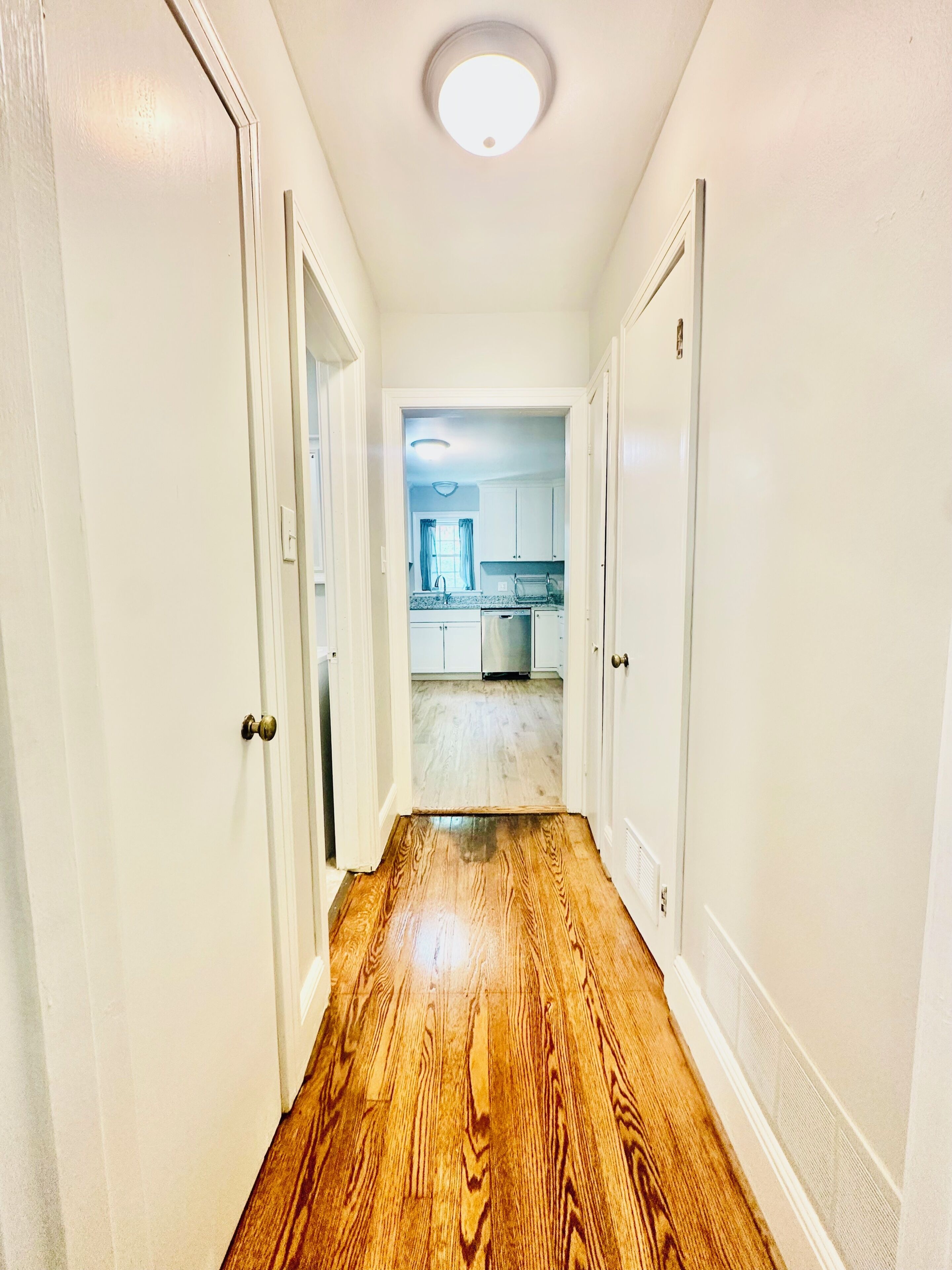 A hallway with wooden flooring leading to a kitchen area.