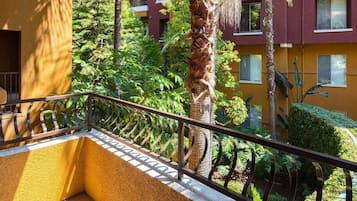 Un balcon doté d’une rambarde en métal, donnant sur un jardin luxuriant où poussent différentes espèces de plantes, ainsi qu’un palmier.