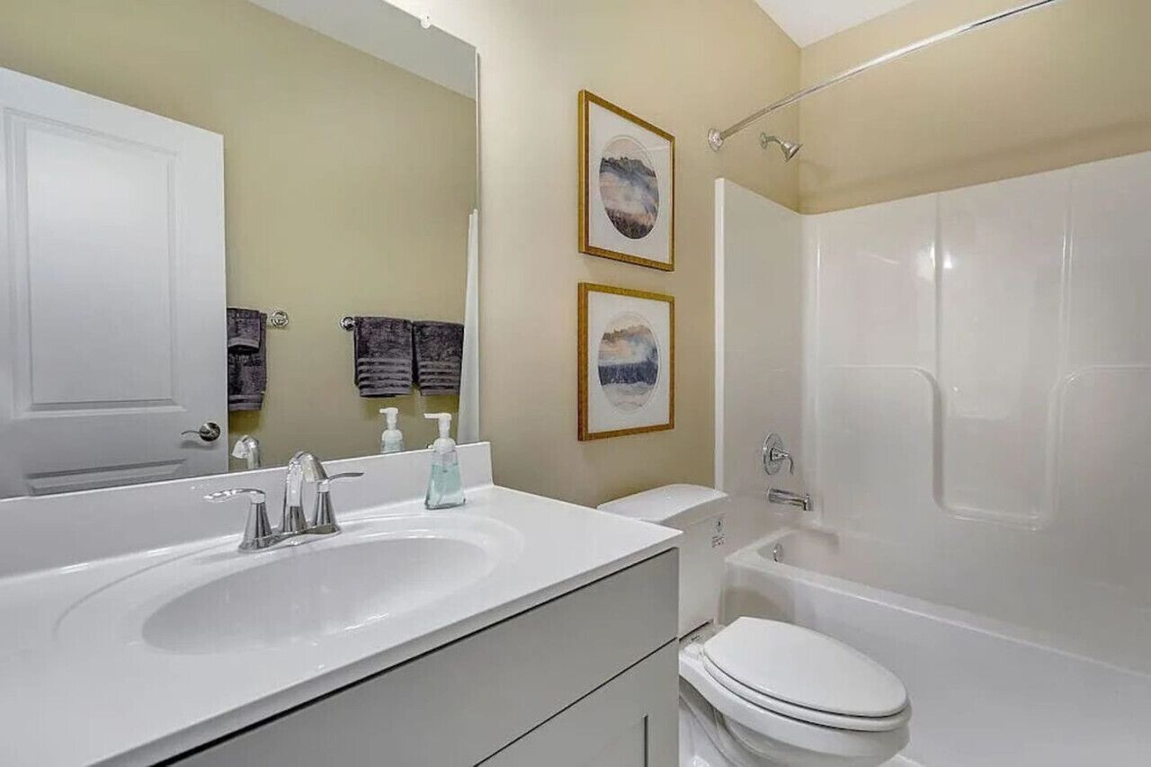 Un baño con lavamanos, inodoro y bañera blancos. Hay dos cuadros en la pared.