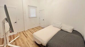 Ein Schlafzimmer mit einem Bett, einem Fenster mit Jalousien, einer Tür und einem Holzboden.