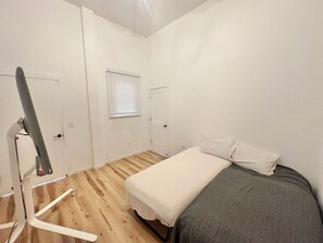 A bedroom with a bed, a window with blinds, a door, and a wooden floor.