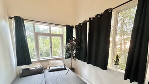 A room with two beds, a potted plant, and a window with curtains.