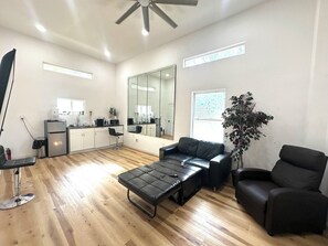 A modern living room with a sofa, a coffee table, and a chair. There is a kitchen area with a refrigerator and a microwave.