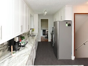 Una cocina estrecha con armarios blancos, encimera de mármol y un refrigerador.