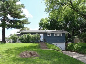 A two-story house with a front porch, a small staircase, and a well-maintained lawn. - Cozy Aksarben Gem 2BR • Quiet • Fenced Yard (Omaha)