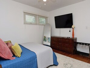 Un dormitorio con cama, cómoda, televisor y ventana con persianas.