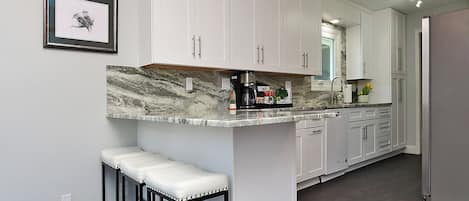 A kitchen with white cabinets, a marble countertop, and a built-in island with stools.
