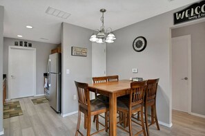 A dining area with a wooden table and chairs, a chandelier, a clock, and a welcome sign. - 2 Condos Adjacent - for groups  4-Night DISCOUNT!! (Branson)
