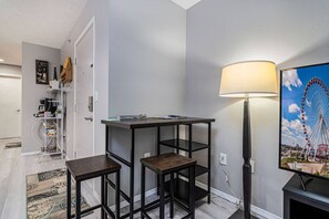 A compact living space with a small table and stools, a lamp, and a wall-mounted TV displaying a Ferris wheel. - 2 Condos Adjacent - for groups  4-Night DISCOUNT!! (Branson)