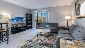 A living room with a sofa, coffee table, TV, bookshelf, and a window with a view. - 2 Condos Adjacent - for groups  4-Night DISCOUNT!! (Branson)
