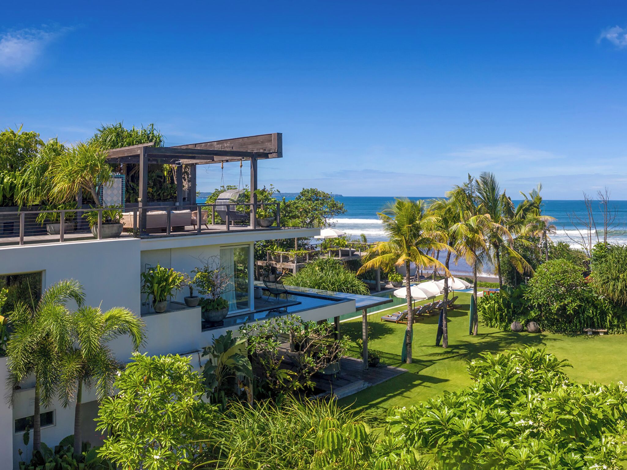 A modern resort with a pool, palm trees, and a view of the ocean.