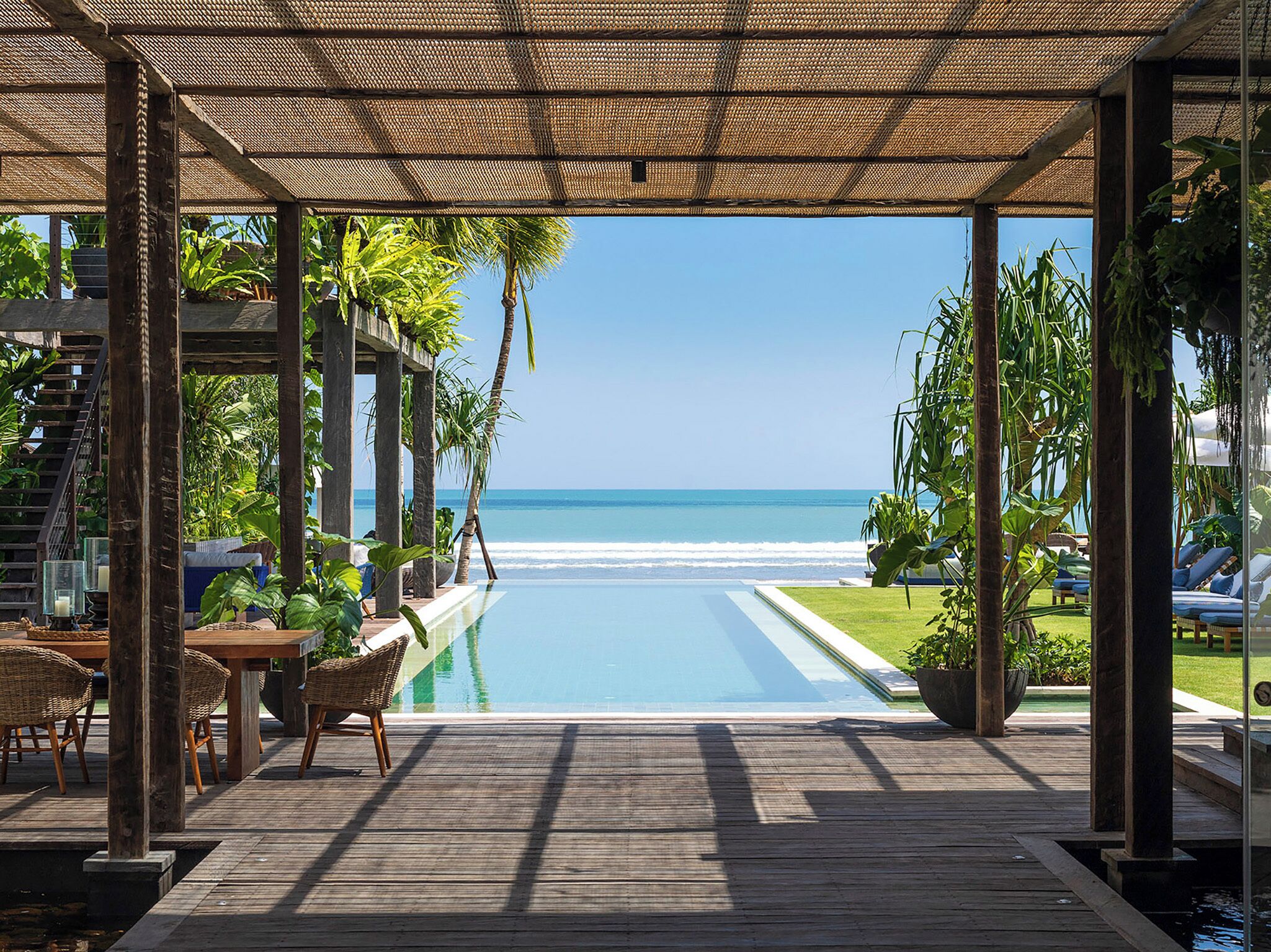 A wooden deck with a pool, overlooking a beach and ocean.