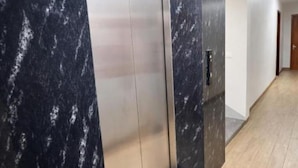 A hallway with a marble wall, a closed elevator door, and a wooden floor. - Hung Phat Hotel Nghe An  (Hung Nguyen)