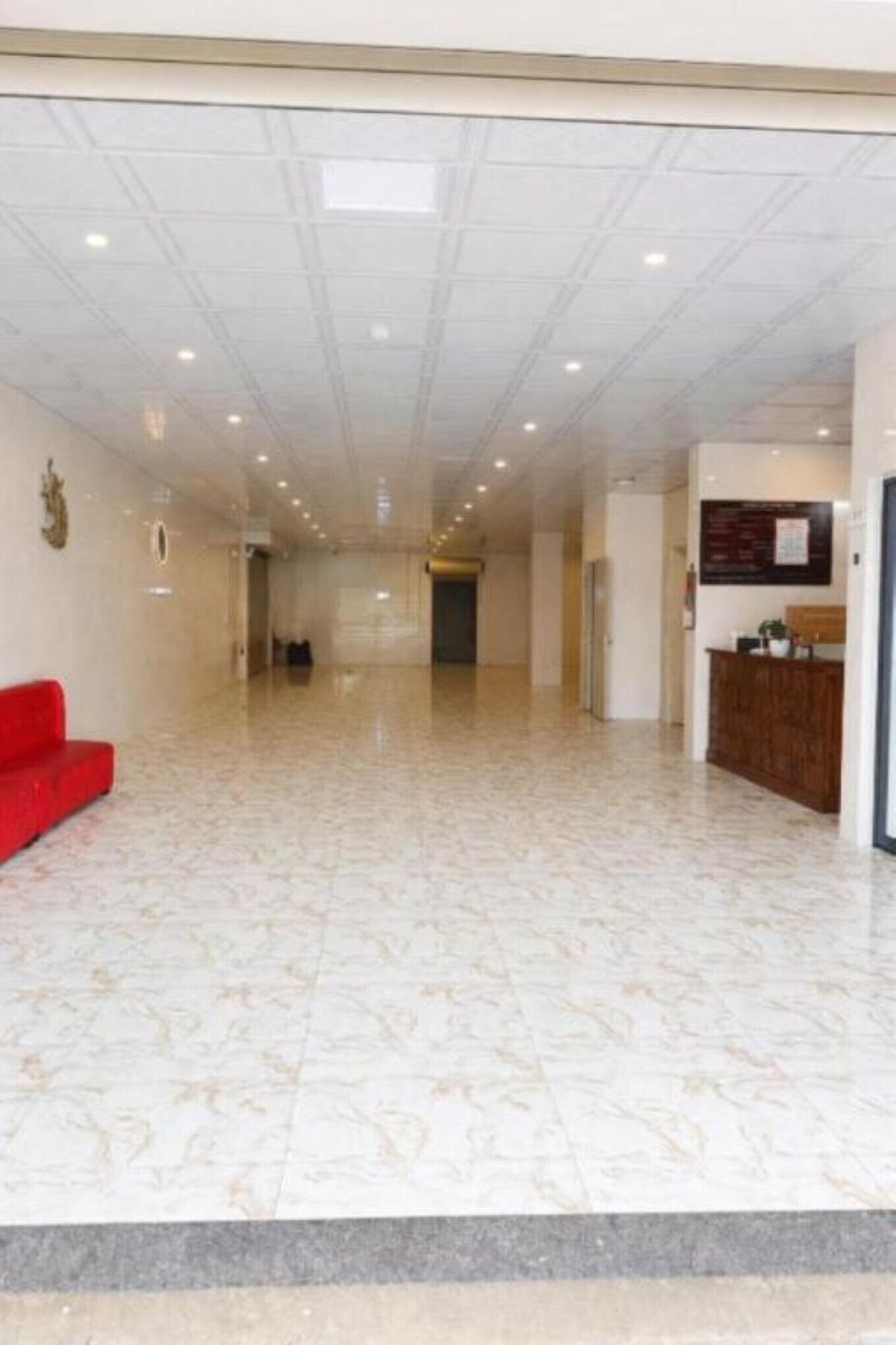 Un hall espacioso con mostrador de recepción, un sofá rojo y suelo estampado.