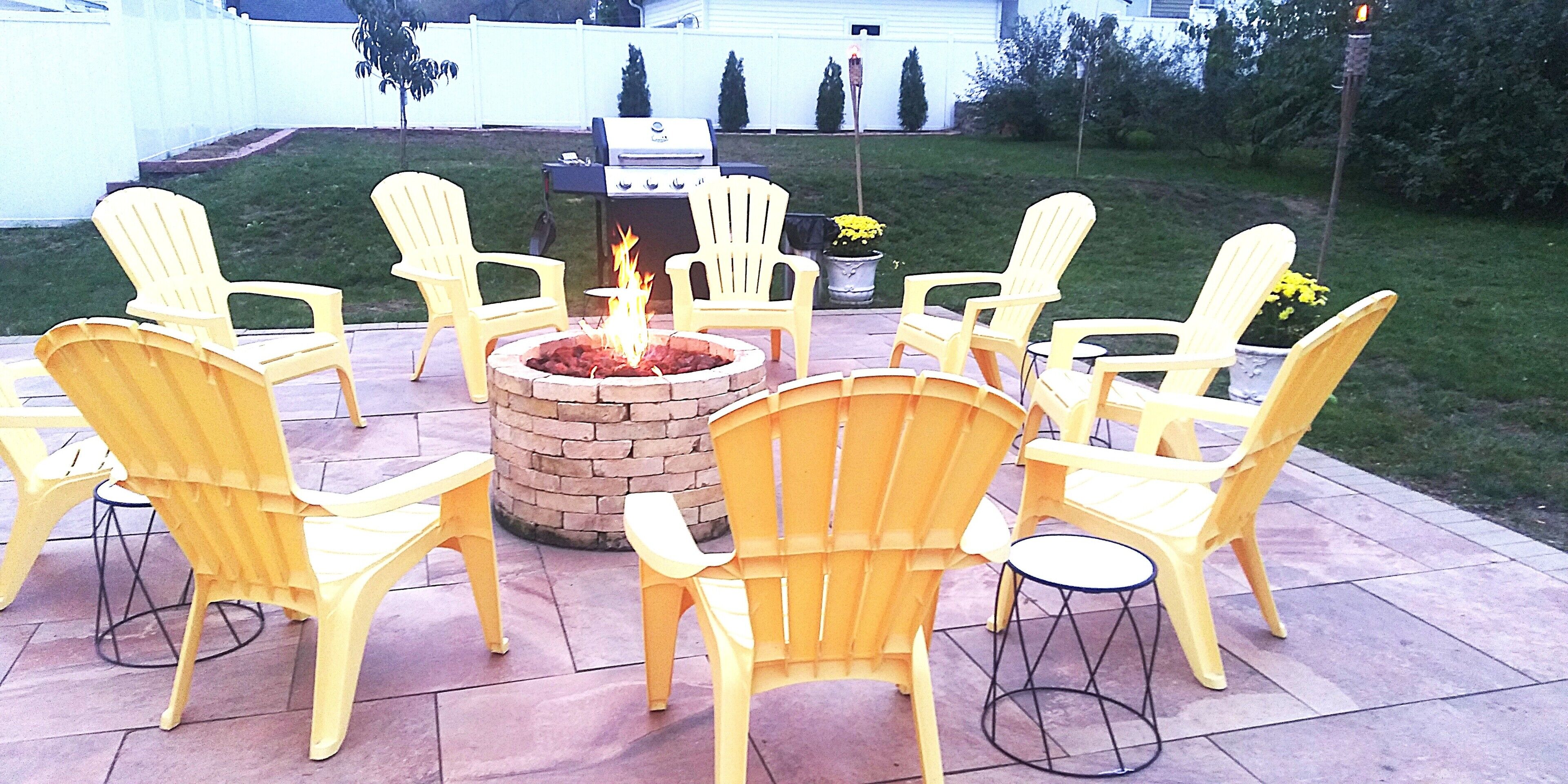 A patio with yellow Adirondack chairs arranged around a fire pit.