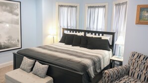 Ein Schlafzimmer mit einem Bett, Nachttischen, einem Sessel und einem großen gerahmten Bild an der Wand.