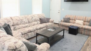 Ein Wohnzimmer mit zwei Sofas, einem Couchtisch, einem Fernseher und einer Tür.