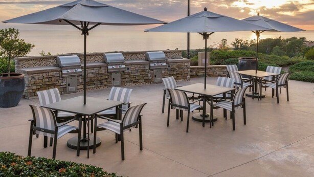 Een terras buiten, met een stenen muur, barbecuegrills en een tafel met stoelen.