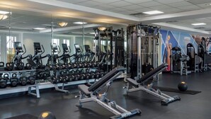 Een fitnessruimte met trainingsapparatuur, spiegels en gewichten.