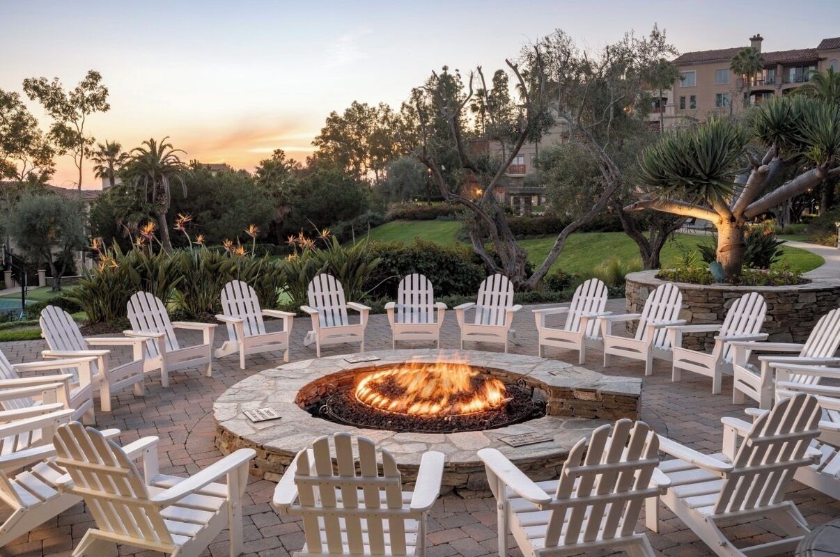 A circular outdoor seating area with a fire pit surrounded by white Adirondack chairs.