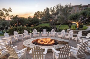A circular outdoor seating area with a fire pit surrounded by white Adirondack chairs.