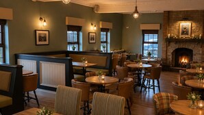 A cozy restaurant with wooden tables and chairs, a fireplace, and framed pictures on the walls.