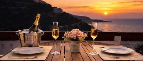 A wooden table set for two with a bottle of champagne, two glasses, and a vase of flowers.