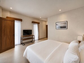 A hotel room with a bed, a TV on a stand, a painting on the wall, and a door with curtains. - Villa SAE VI (Badung)