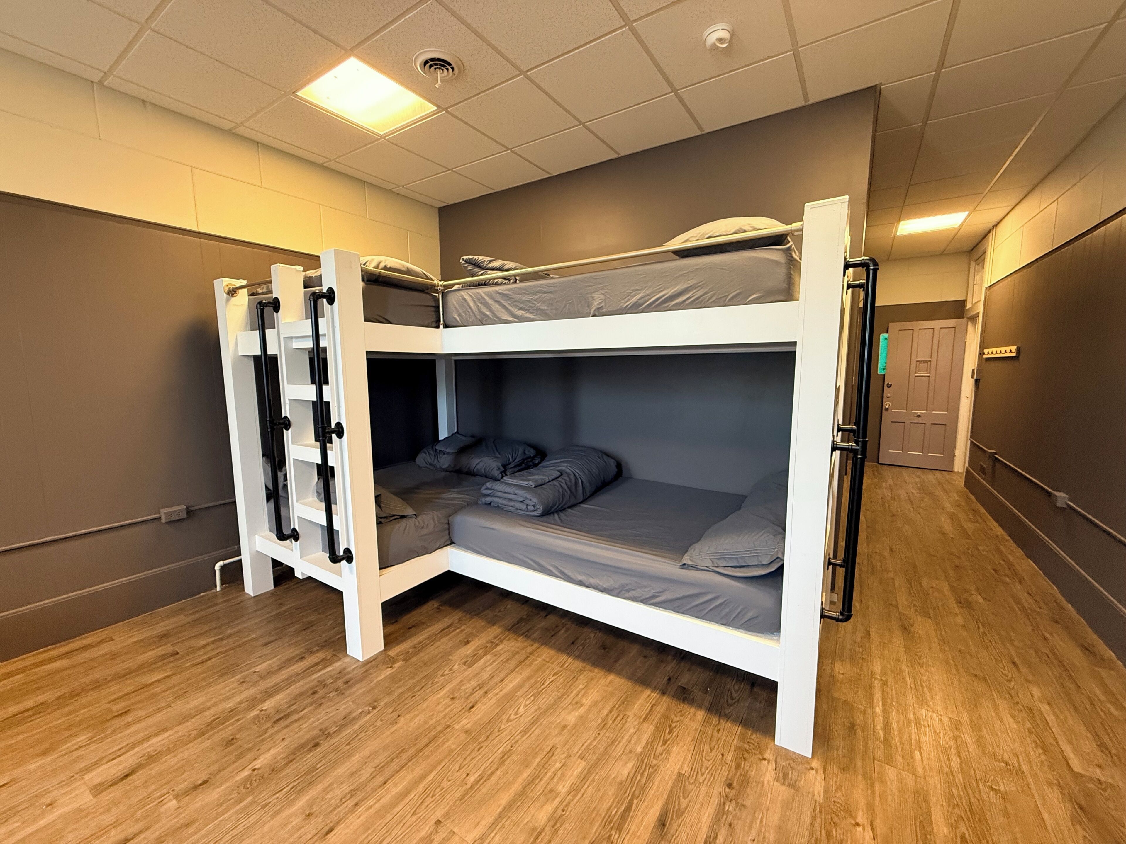 Une chambre avec un lit superposé, une échelle, un plancher en bois et une porte visible au fond.