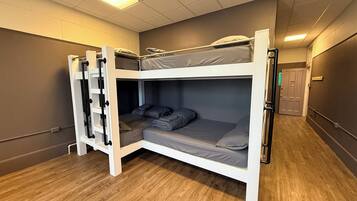 Une chambre avec un lit superposé, une échelle, un plancher en bois et une porte visible au fond.
